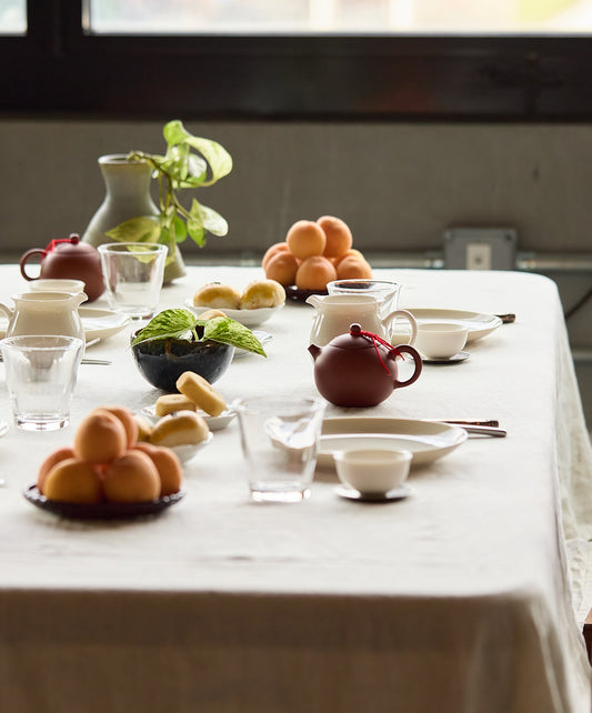 Close-up of a dining table with apricots, bread, teapots, and potted plants arranged neatly.