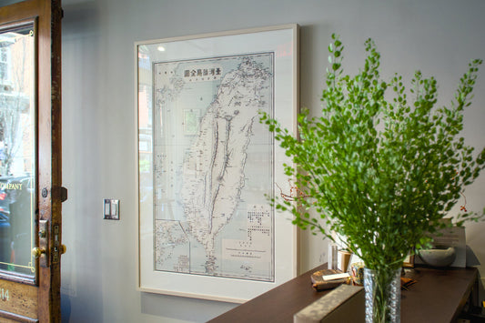 Framed map on a wall with a vase of greenery on a table below.