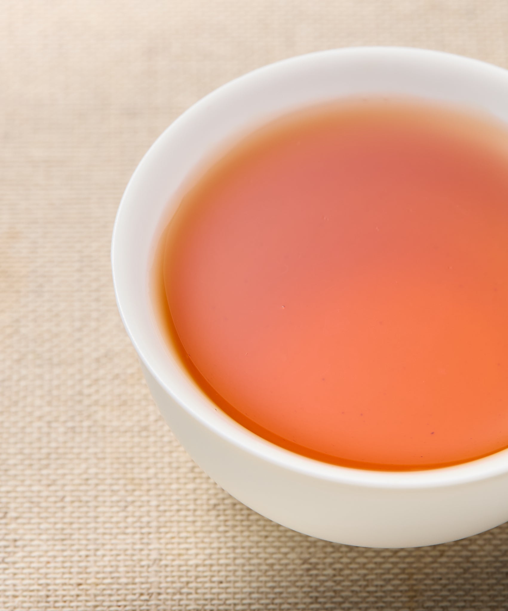 A cup filled with amber-colored tea, placed on a beige fabric surface.