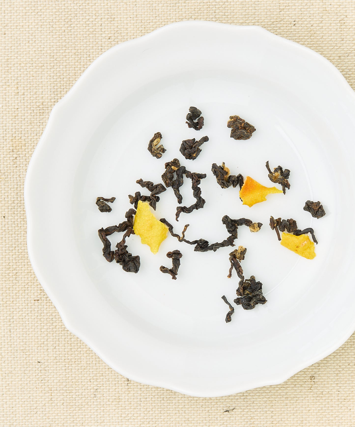 Loose black tea leaves mixed with bright citrus peels scattered on a white plate.