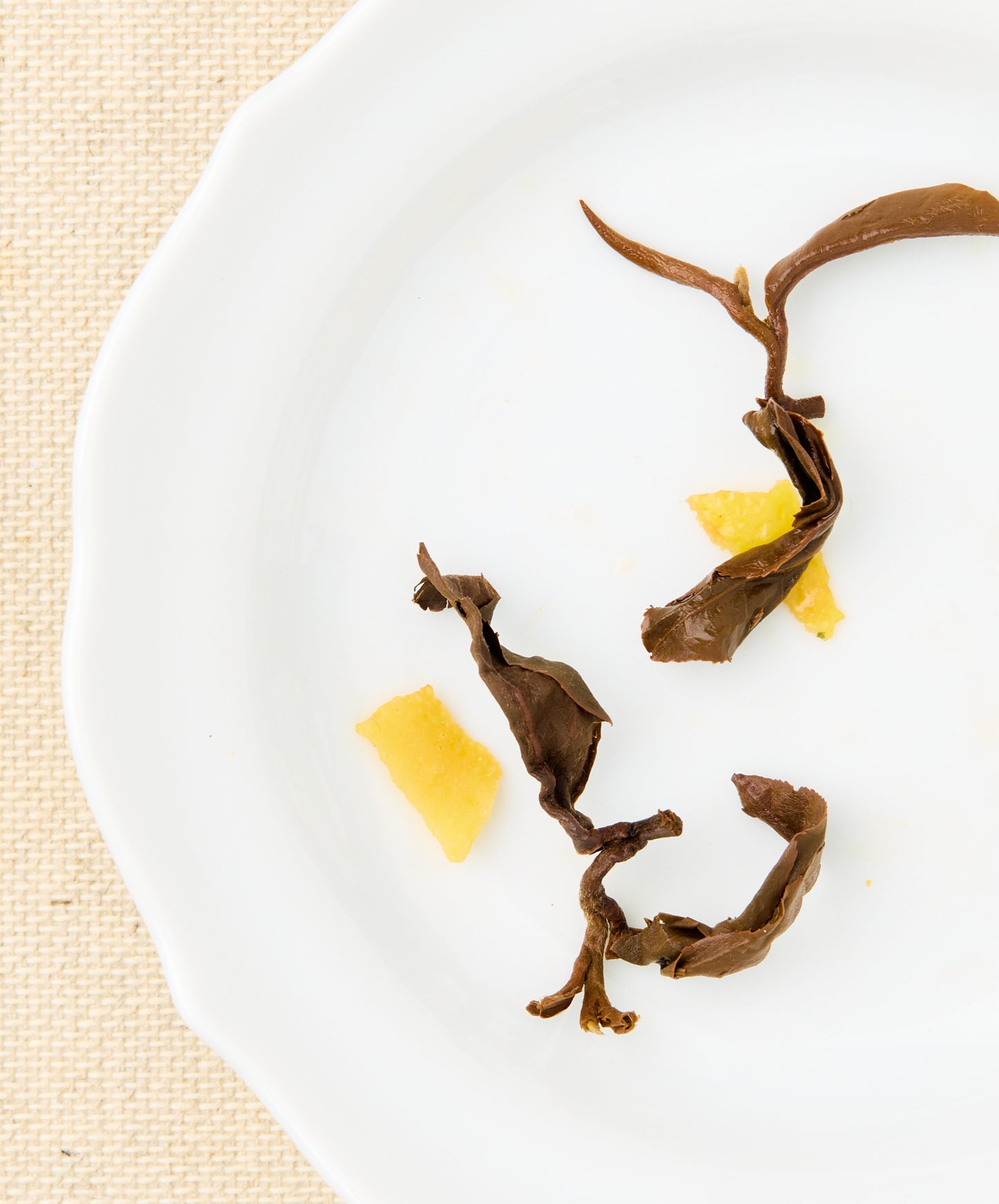 Close-up of steeped tea leaves and citrus peels on a white plate.