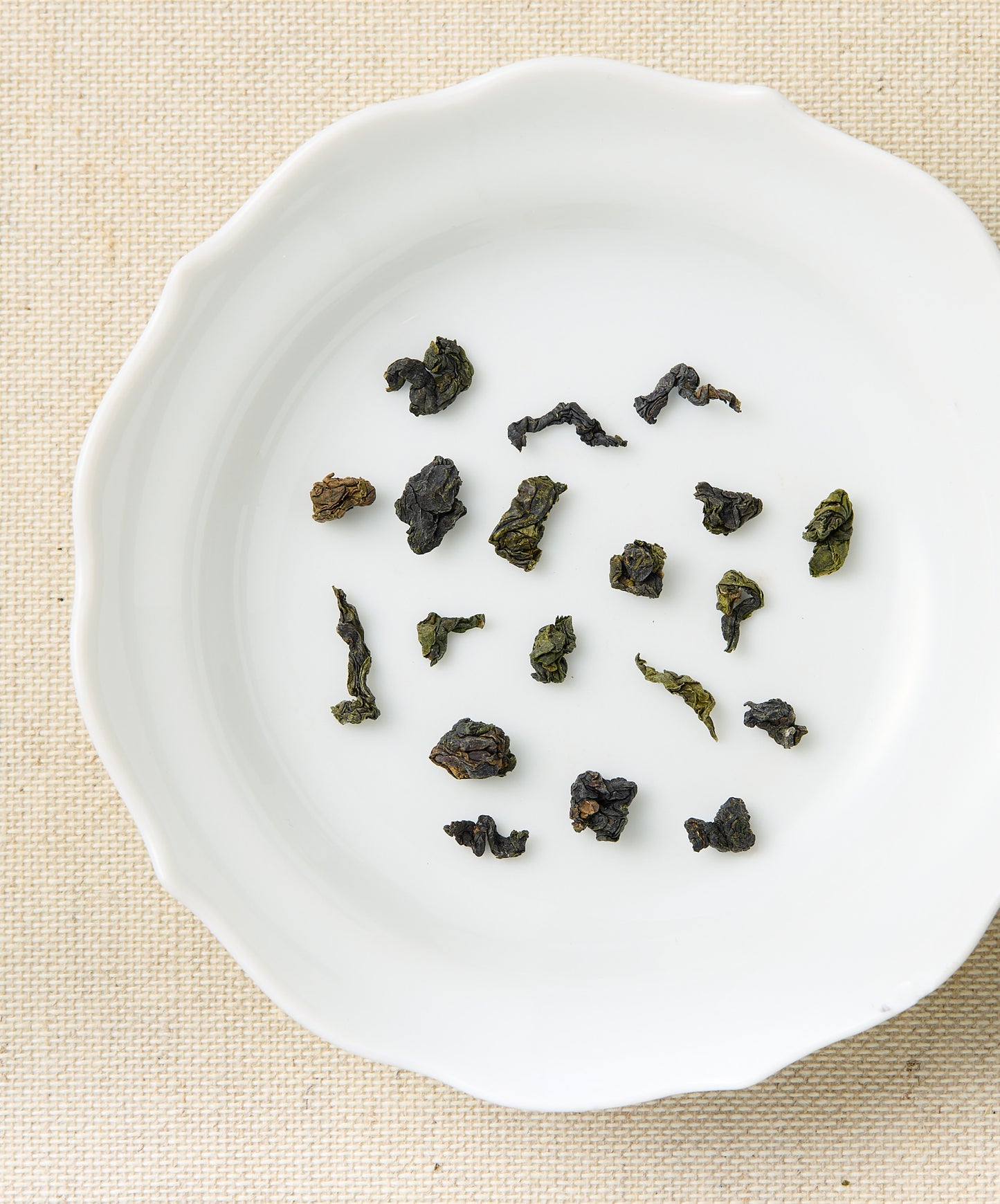 Dried tea leaves on a white ceramic plate with a beige background