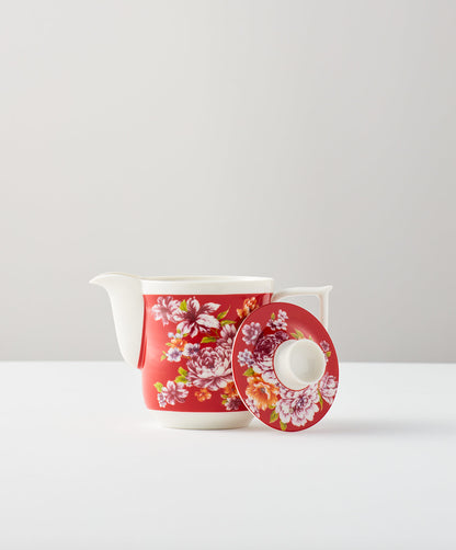 Red floral teapot on a white surface, lid removed