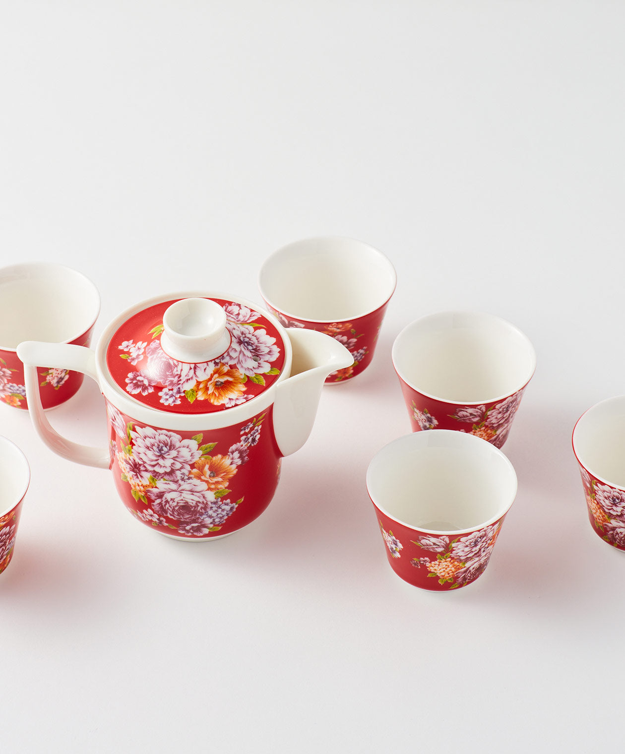 Top view of a red floral teapot surrounded by six matching cups.