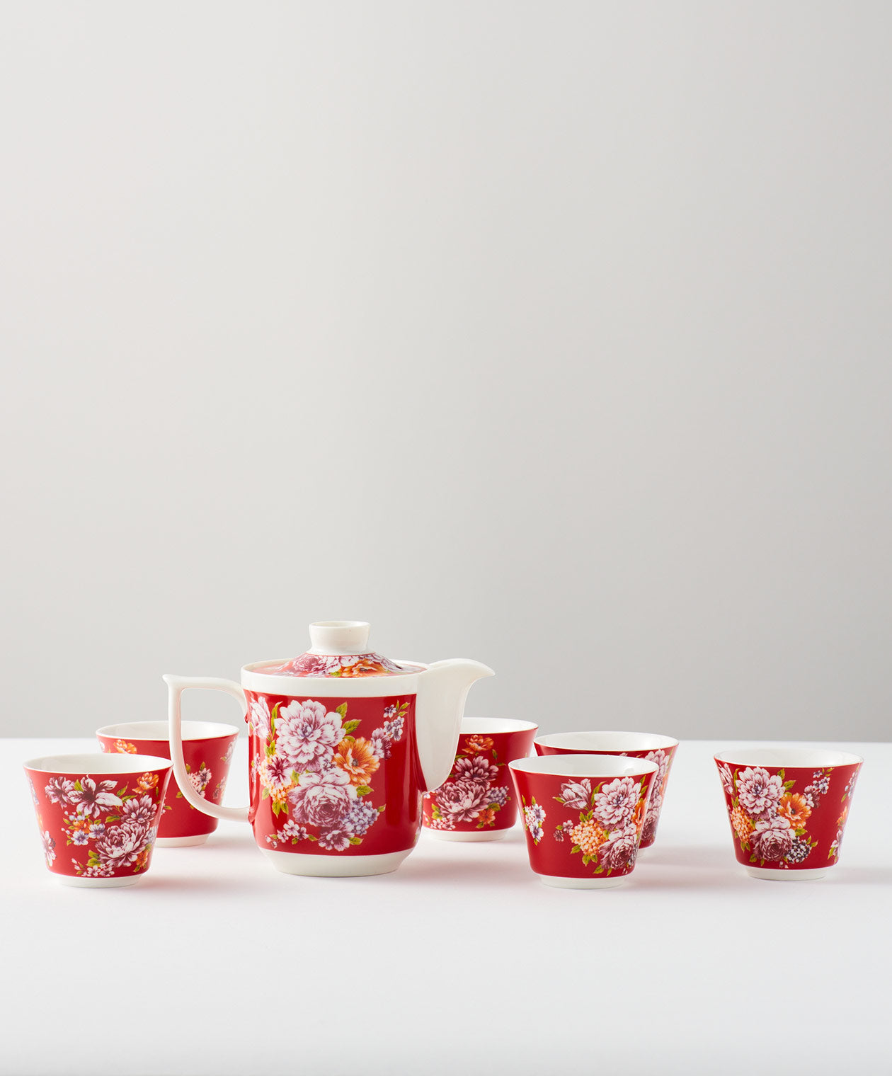 Red floral teapot with six matching cups on a white surface