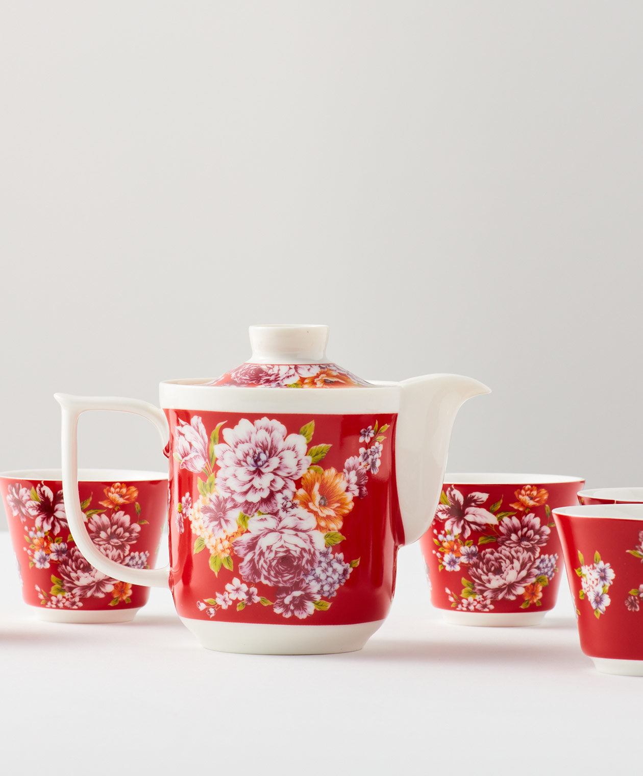 Close-up of a red floral teapot with matching cups.