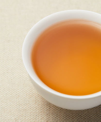 A close-up of amber-colored tea in a white teacup on a textured beige background.