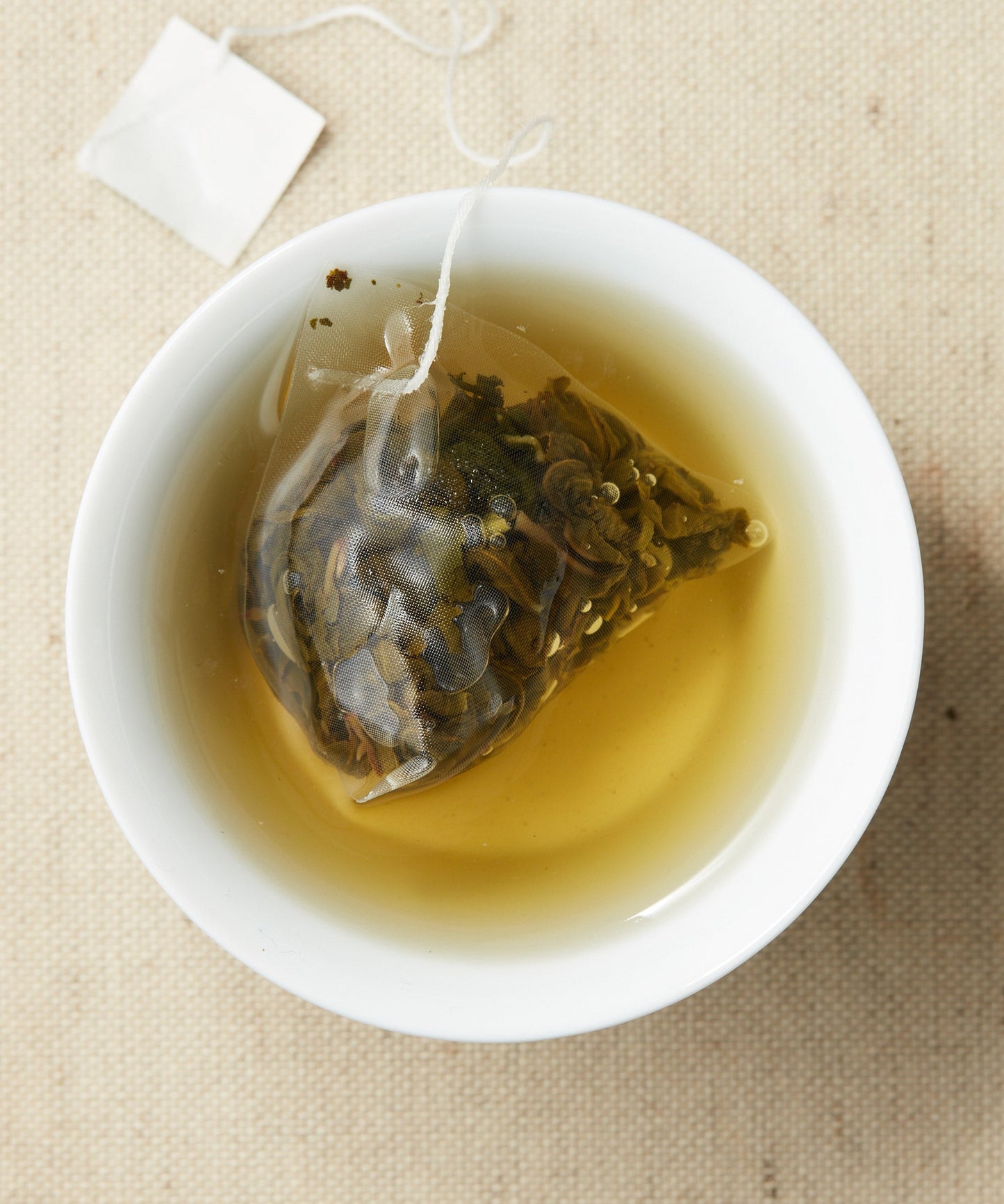 A cup of steeped tea with a pyramid-shaped tea sachet containing loose leaves, submerged in the liquid.