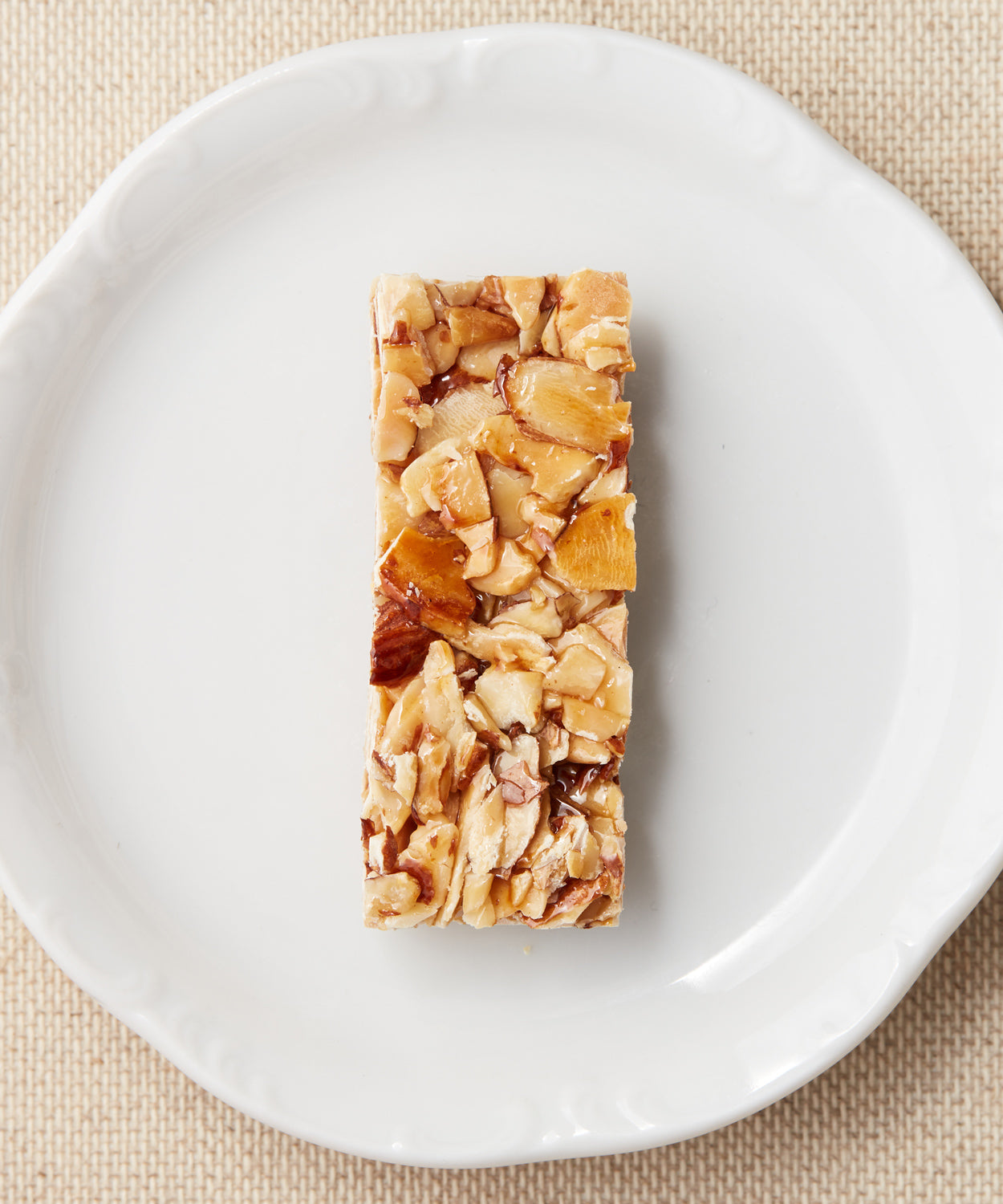 A rectangular bar made with chopped almonds bound in syrup, displayed on a white plate.