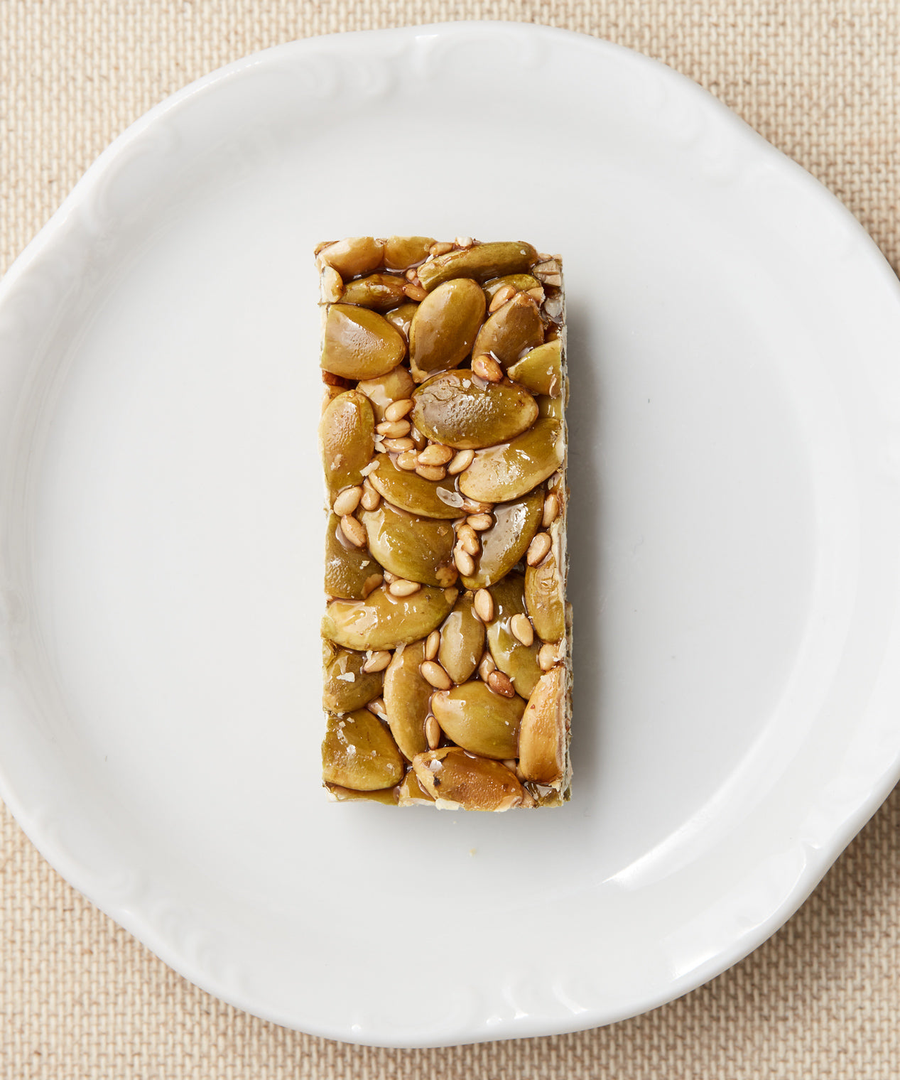 A rectangular bar made with pumpkin seeds and sesame seeds bound in syrup, displayed on a white plate.